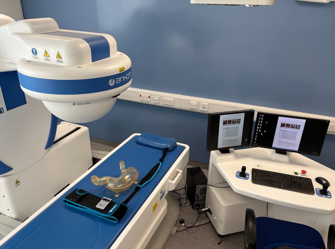 Figure 3. Magnet-controlled capsule endoscopy system showing magnet robot, data recorder and belt, plastic stomach model and control station with joysticks and monitors.